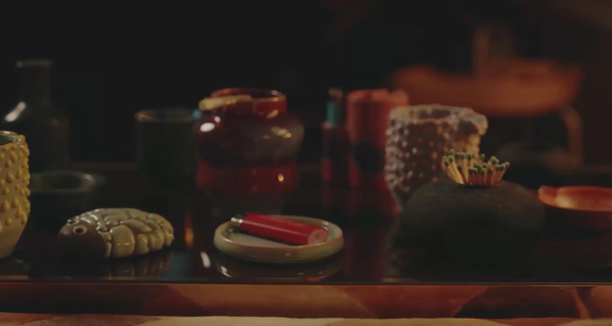 A low table downstairs at night: ceramic ashtrays, a red lighter on a small plate, matches in a stone holder