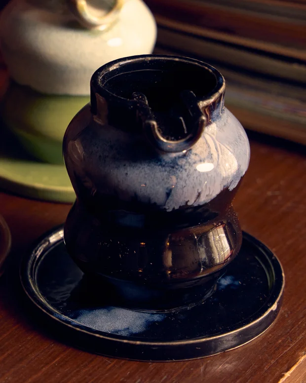 A dark glazed wavy ashtray on its plate, on a wooden shelf