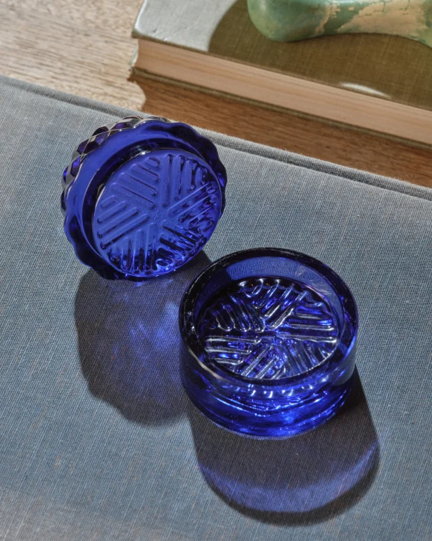 A cobalt blue cut-glass grinder, opened in two halves, casting blue shadows