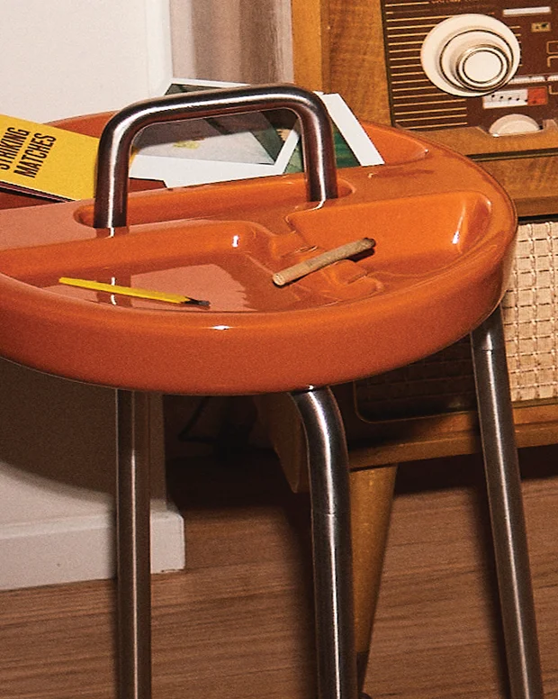 An orange side table ashtray with a steel handle next to a vintage radio