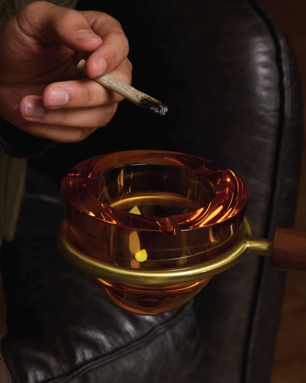 A hand rolling over an amber glass ashtray on a brass arm