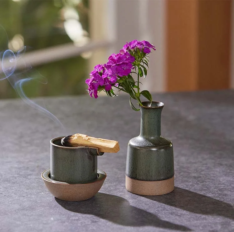 A grey-green ashtray with a rolled joint resting in its notch, next to a matching vase of purple flowers