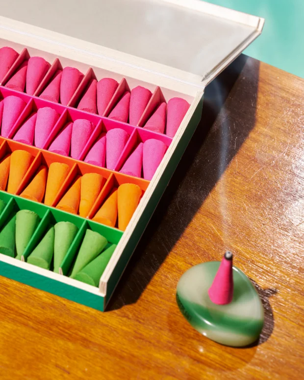 An open box of pink, orange and green incense cones beside a green marble burner with a smoking cone