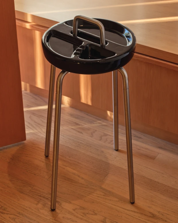 A black side table ashtray on steel legs in a wood-panelled room