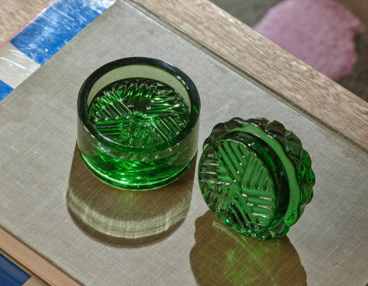 A green cut-glass grinder, lid off, on a linen-covered book