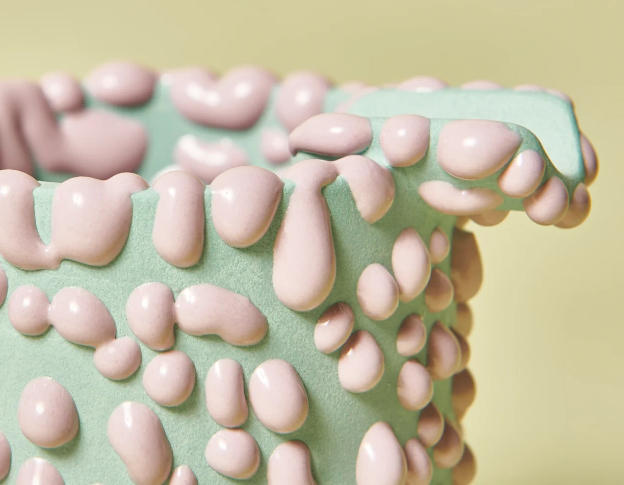 Close-up of a mint ceramic surface covered in raised pink gloops of glaze